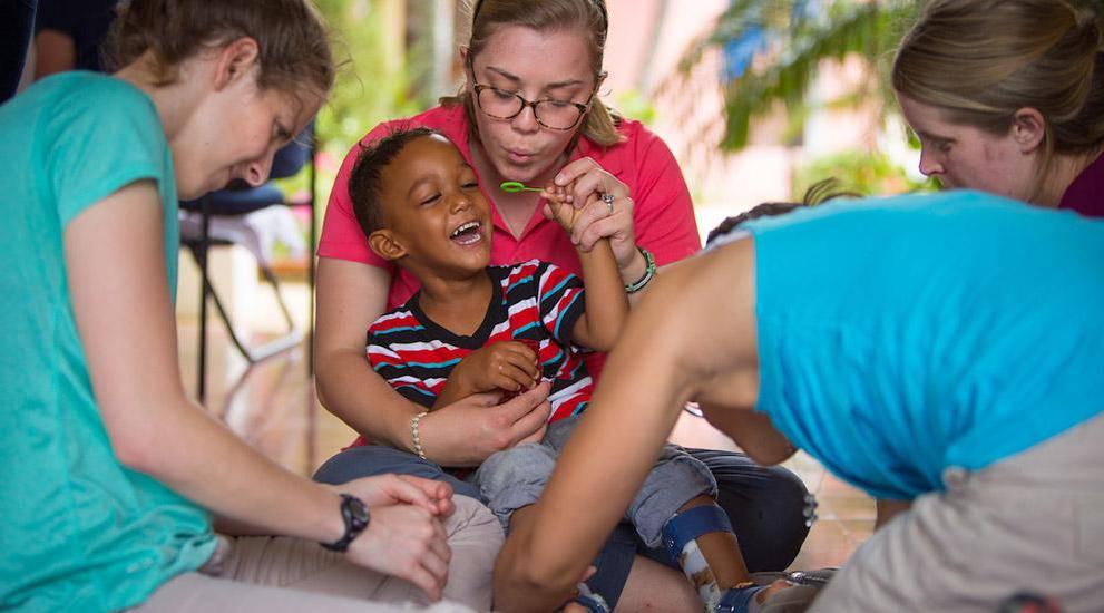 Students in the Encuentro Dominicano program helping a young boy with leg braces